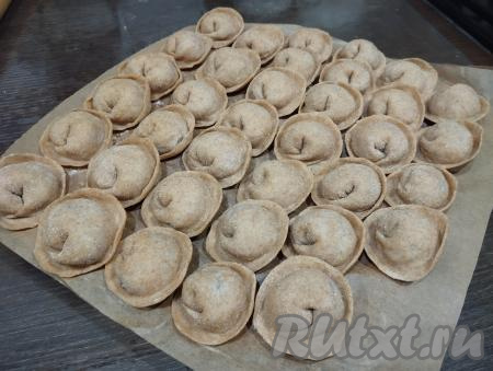 Постепенно формируем все пельмени. Всего у меня получились 96 пельменей из цельнозерновой муки. Часть пельменей можно заморозить впрок, для этого разделочную доску застилаем бумагой для выпечки (или припыляем мукой). Выкладываем на подготовленную доску пельмени в один слой и отправляем в морозилку. Когда пельмени полностью замёрзнут, перекладываем их в полиэтиленовый пакет и храним в морозилке. По мере необходимости, не размораживая, отвариваем замороженные пельмени.