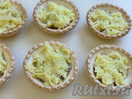 Варёную картошку очистить, натереть на крупной тёрке, выложить в тарталетки поверх селёдки и слегка утрамбовать чайной ложкой.