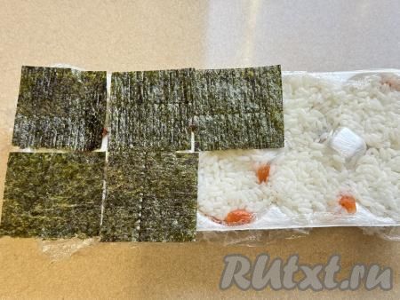 Листы нори нарезать на квадратики, размер которых должен быть равен размеру ячеек для яиц. Выложить квадраты нори поверх риса, слегка прижать.