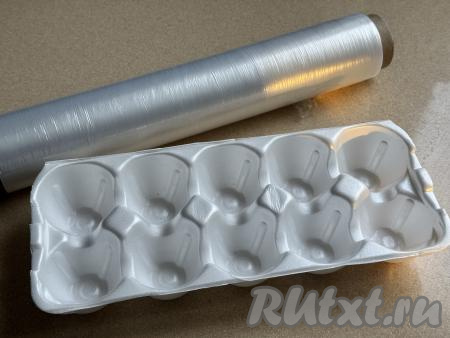Форму с ячейками из-под яиц застелить пищевой плёнкой так, чтобы плёнка свисала с краёв формы.