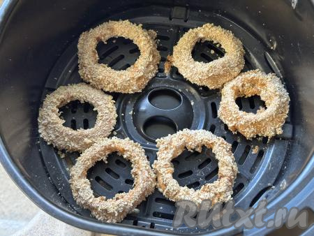 Готовые луковые кольца, покрытые хрустящим кляром, переложить из чаши аэрогриля на тарелку. Постепенно покрыть кляром и запечь все кольца. За один раз все колечки в чашу аэрогриля не помещаются, поэтому запекать их нужно в несколько заходов.