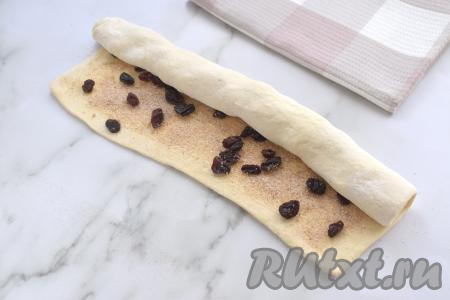 Начиная с более длинной стороны, сворачиваем тесто с изюмом в рулет.