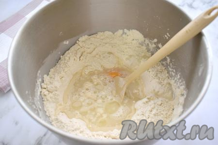 В центр мучной смеси вливаем тёплую воду, растительное масло и вбиваем туда же куриное яйцо.