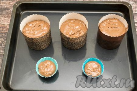 Разложить шоколадное тесто для куличей по бумажным формам, заполняя формы не более, чем на 2/3 высоты. Я заполнила 3 формы диаметром 9 сантиметров, остатки теста я разложила в две силиконовые формочки для маффинов. Формы с тестом поставить на противень.