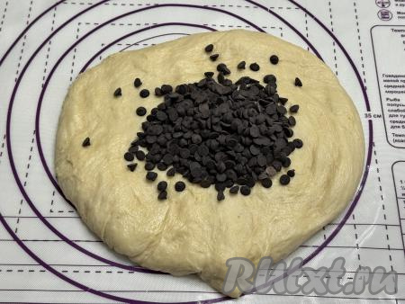 Выложить дрожжевое тесто на рабочую поверхность, присыпанную мукой, добавить шоколадные капли. Тщательно вмешать руками капли в тесто для кулича.