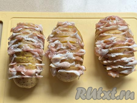 Ломтики бекона нарезать на кусочки подходящего размера, вставить в прорези картошки.&nbsp;