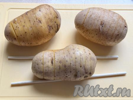 На каждой картофелине сделать надрезы, не дорезая до конца, чтобы получилась "гармошка". Для того чтобы не прорезать картошину до конца, я с двух сторон клубня кладу ограничители (этот могут быть, например, палочки или вилки), как на фото, и сверху картошины делаю надрезы. Ограничители не дают прорезать картофелину ножом до конца. 