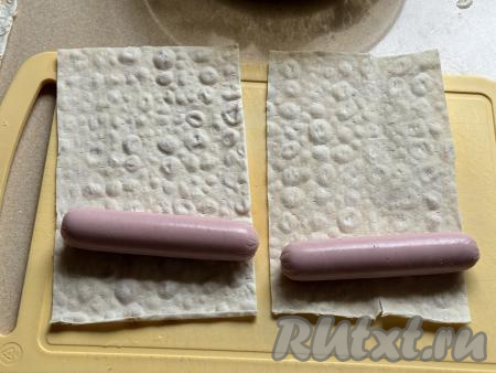 Лаваш нарезать на прямоугольники. Ширина нарезанных заготовок лаваша должна быть примерно с сосиску. Сосиски очистить от слюды и выложить на край лаваша.