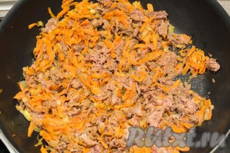 В сковороду с обжаренными овощами добавить размятые кусочки тушёнки. Перемешать тушёнку с морковкой и луком, равномерно распределяя мясо по овощам. Обжарить, периодически перемешивая, в течение 3-4 минут.
