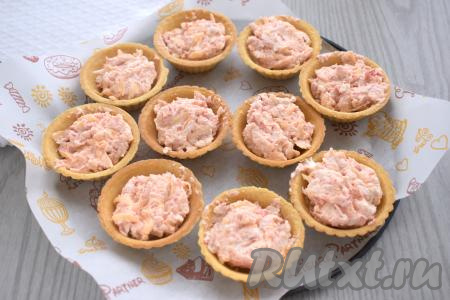 Песочные тарталетки наполняем начинкой из крабовых палочек, творожного сыра, икры и твёрдого сыра. Я наполнила 10 тарталеток. Форму для запекания (или противень), по желанию, застилаем пергаментом, затем расставляем тарталетки с начинкой и отправляем в духовку, разогретую до 180 градусов, на 8-9 минут (до появления на поверхности небольшой аппетитной корочки).