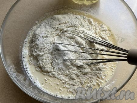 Отмерить и просеять в отдельную миску муку. В миску с яично-молочной смесью всыпать весь разрыхлитель и половину муки. Перемешать тесто венчиком, чтобы оно стало однородным, без комочков. Далее подсыпать в тесто оставшуюся муку по 0,5 столовой ложки, тщательно перемешивая венчиком после добавления каждой порции муки и контролируя густоту замешиваемого теста.