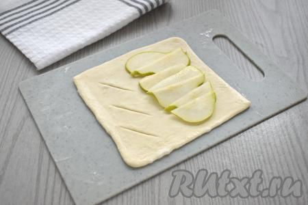 Берём первый получившийся квадрат из теста, зрительно делим его на 2 равных части. Грушу, по желанию, очищаем от кожуры (я очищать от кожуры не стала), нарезаем на тонкие ломтики, вырезая сердцевину с косточками. На одну половину квадрата выкладываем немного внахлёст 1/4 часть ломтиков груши, отступая от краёв теста по 1-1,5 сантиметра. На второй половине квадрата делаем разрезы, как на фото, тоже не забывая отступить от краёв теста.