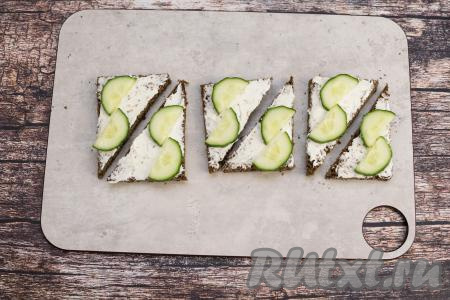 Поверх хлеба, смазанного творожным сыром, выложить, как на фото, по кружочку свежего огурца, разрезанного на 2 половинки.