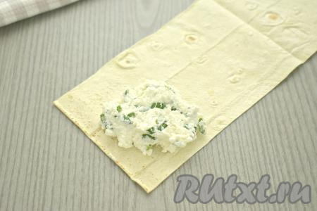 Ближе к одному из узких краёв полоски из лаваша, как на фото, выкладываем 2 столовых ложки начинки из творога и зелени. Старайтесь, выкладывая начинку, отступать от краёв лаваша не менее 1 сантиметра.