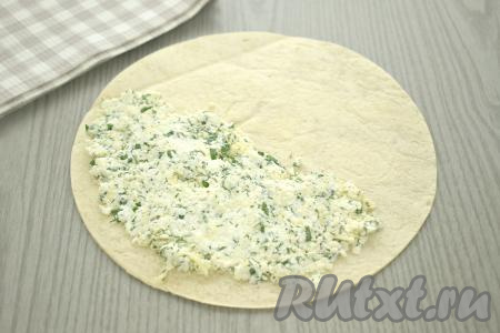 Раскладываем лепёшку на столе. Я купила тортилью, диаметр которой был больше диаметра чаши моего аэрогриля. Поэтому я достала решётку из аэрогриля, приложила её к лепёшке и лишнее отрезала с помощью кулинарных ножниц. В результате у меня получилась тортилья диаметром 18 сантиметров. Зрительно делим лепёшку на 2 равных части. На одну половину выкладываем начинку из творога и сыра, разравниваем, отступая от краёв тортильи примерно по 1 сантиметру.