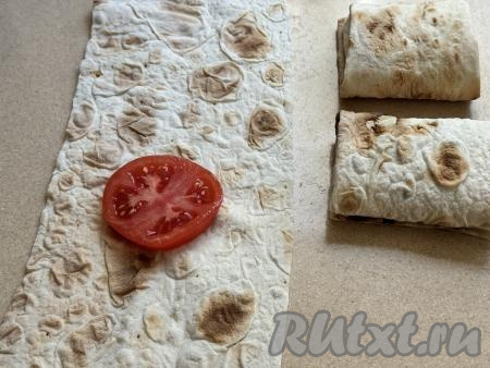 Кухонными ножницами нарезать лаваш на прямоугольные полоски размером 25 сантиметров на 15 сантиметров. У меня получились 9 полосок. Ближе к одному из узких краёв лаваша, немного отступив от длинных краёв, выложить кружок помидора.&nbsp;