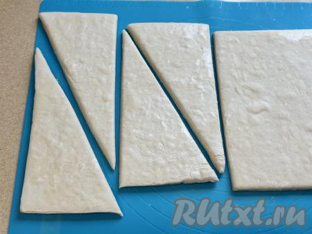 Каждый разморозившийся пласт слоёного теста, не раскатывая, нужно разрезать на 2 одинаковых прямоугольника, а затем каждый прямоугольник разрезать по диагонали. В результате из двух пластов теста у нас получатся 8 треугольных заготовок.