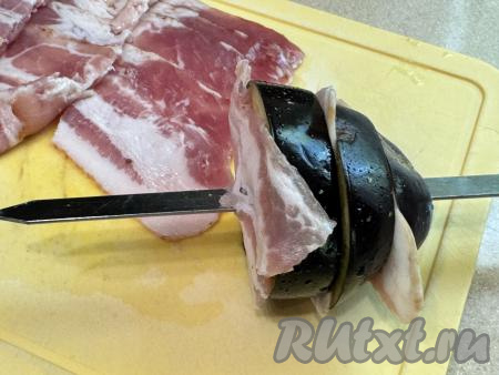 Натереть каждый кружочек баклажана маслом, солью и специями со всех сторон. Я купила бекон, уже нарезанный на тонкие полоски. Если вы купили целый кусок бекона, тогда вначале нарежьте его на тонкие полоски. Полоски бекона нарезать на кусочки, размер которых должен быть чуть больше диаметра баклажана. На шампуры надеть кружочки баклажана, чередуя с кусочками бекона. Бекон должен достаточно плотно прилегать к баклажанам, чтобы во время жарки на мангале жир, выделяющийся из бекона, впитывался в баклажаны.
