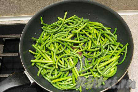 На сковороде разогреть растительное масло. В горячее масло выложить нарезанные чесночные стрелки. Обязательно следите, чтобы на стрелках не было воды, так как вода вступает в реакцию с разогретым маслом и может привести к сильному разбрызгиванию масла и даже к кратковременному его воспламенению.