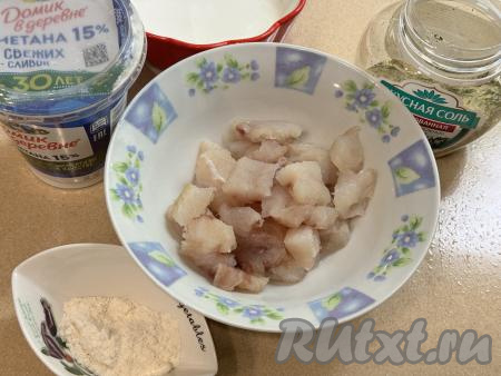 Подготовить продукты для приготовления филе минтая в сметане в аэрогриле. Я для этого блюда купила филе минтая, уже отделённое от костей, его нужно будет полностью разморозить, промыть водой, обсушить. Но можно взять целые тушки минтая, разморозить их, убрать кожу, отрезать плавники и хвост, удалить хребет вместе с внутренностями и костями, промыть водой, обсушить и у вас будет отличное филе минтая. Нарезать филе минтая на кубики с размером стороны 1,5 сантиметра, выложить в миску. 