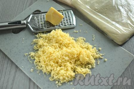 Достаём из морозилки слоёное тесто, даём ему разморозиться. Для формирования сырных косичек можно взять как слоёное дрожжевое тесто (его я и использовала), так и слоёное бездрожжевое тесто. После того как тесто разморозится, натираем сыр на мелкой тёрке.