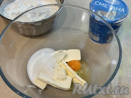 Подготовить продукты для приготовления калачиков на сметане в духовке. Сливочное масло заранее достать из холодильника, дать полежать при комнатной температуре, чтобы оно согрелось и стало мягким. В миску всыпать сахар, вбить сырое яйцо, выложить мягкое масло, нарезанное на кусочки.&nbsp;