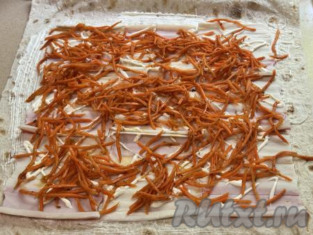 Корейскую морковку отжать от лишнего маринада, длинные полоски нарезать на части. Равномерно распределить морковь поверх крабовых палочек.&nbsp;