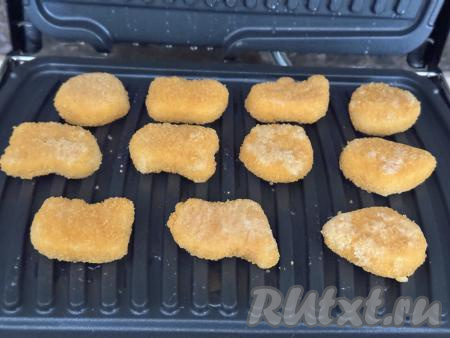 Электрогриль разогреть на режиме "Мясо". Хорошо смазать створки электрогриля растительным маслом и выложить наггетсы, чтобы они не плотно лежали к друг другу и оставались зазоры.&nbsp;Закрыть створки электрогриля.&nbsp;Не прижимайте верхнюю створку электрогриля слишком сильно, чтобы из наггетсов не вытек сок и не раздавилась панировка.