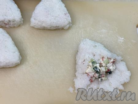 Аккуратно подворачивая края лепёшки из риса на начинку, как на фото, завернуть начинку в рис. Чтобы в процессе формирования онигири рис не прилипал к рукам, можно смочить руки водой.