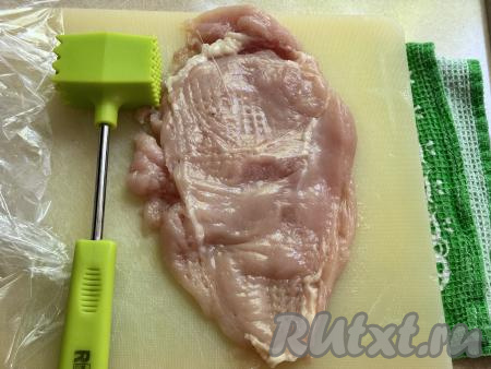 Выложить кусочки филе на разделочную доску, накрыть пищевой плёнкой и отбить мясо кулинарным молотком до толщины 0,5 сантиметра.