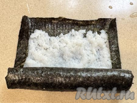 Свернуть лист нори с рисом в тугой рулет, начиная с любой из двух неподвёрнутых сторон.