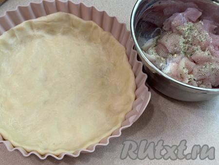 Куриное филе промыть водой, обсушить, нарезать на кубика с размером стороны 1,5 сантиметра, выложить в миску. Посолить мясо, приправить специями (в качестве специй я добавила соль, смешанную с сушёными чесноком и зеленью). 50 грамм сливочного масла достать из холодильника, дать ему согреться и немного размягчиться при комнатной температуре. По прошествии часа достать охладившееся тесто из холодильника, разделить на 2 примерно равных части. Одну часть теста на слегка присыпанной мукой поверхности раскатать в круг, выложить в форму диаметром 26 сантиметров (у меня - силиконовая форма), сформировать бортик высотой примерно 3 сантиметра.&nbsp;