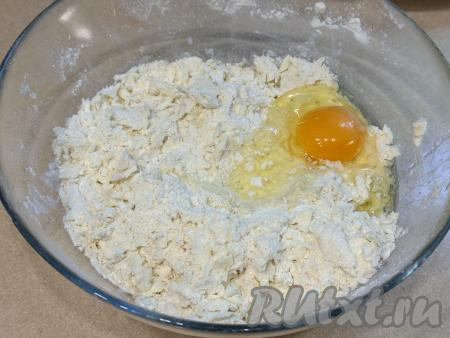 Перетереть массу руками до получения мелкой крошки. Затем добавить сырое яйцо и 50 миллилитров холодной воды. Начать замешивать тесто столовой ложкой (или вилкой), а затем, подсыпая по мере необходимости оставшуюся муку, продолжить вымешивать его руками, собирая в ком.