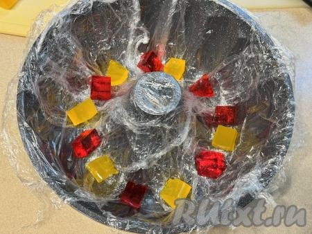 Форму для формирования торта застелить пищевой плёнкой так, чтобы концы плёнки свисали с краёв формы. Выложить на дно формы несколько кубиков желе. Я взяла форму для кексов с отверстием по середине диаметром 28 сантиметров.