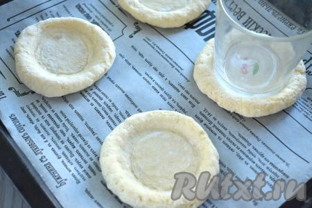 Замешанное творожное тесто делим на 4 равных части (у меня вес каждого кусочка теста получился примерно 70 грамм). Из каждой части теста формируем лепёшку диаметром 9 сантиметров. Получившиеся лепёшки выкладываем на противень, застеленный пергаментом.&nbsp; Я застелила противень силиконизированным пергаментом, к нему ничего не пристаёт в процессе выпечки, если вы не уверены в качестве пергамента, тогда перед выкладыванием творожных лепёшек слегка смажьте его растительным маслом. С помощью дна стакана делаем в центре каждой лепёшки углубление. Если стакан будет сильно липнуть к тесту, тогда можете немного обмакнуть дно стакана в муку.