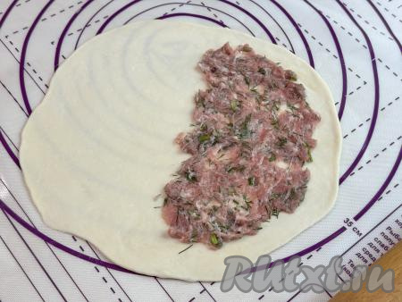 На присыпанной мукой поверхности раскатать каждую часть теста в круг диаметром примерно 19 сантиметров. На одну половину круга, отступая от краёв круга по 1 сантиметру, выложить одну часть начинки, аккуратно распределить. Начинка должна лежать тонким слоем.