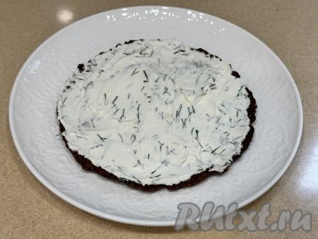 На плоскую тарелку выложить первый печёночный блин, смазать его 1/4 частью творожного сыра, смешанного с зеленью, разровнять. 