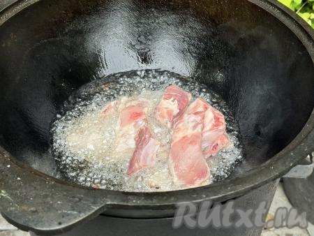 Казан установить на костёр, влить растительное масло. Как только масло закипит, выложить свиные рёбрышки в казан.