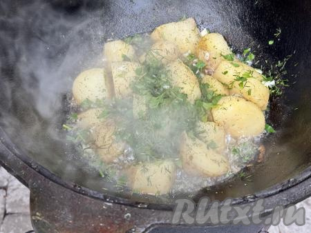 В казан с готовой картошкой добавить зелень и чеснок, перемешать.