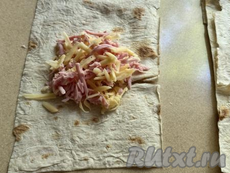 Начинку из колбасы и сыра зрительно разделить на 6 равных частей (по количеству прямоугольных заготовок из лаваша). Взять первую заготовку из лаваша, выложить одну часть начинки ближе к одной из узких сторон, не забывая отступать немного от краёв лаваша.