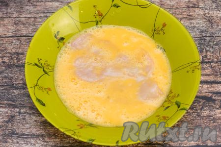 В тарелку со взбитыми яйцами выложить одну куриную отбивную, покрыть мясо яичным кляром с двух сторон.
