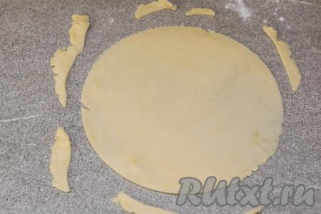 Из холодильника достать первый шарик из теста. На припылённой мукой поверхности раскатать шарик из песочного теста до толщины примерно 2 миллиметра. Для того чтобы подравнять края теста (нам нужно получить круг из теста), нужно поверх раскатанного теста выложить перевёрнутую тарелку (я взяла тарелку диаметром 19,5 сантиметров), обрезать ножом края теста, формируя круг.