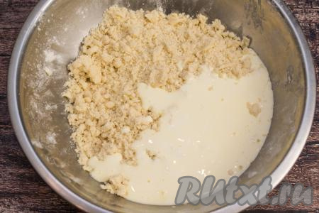 Получившуюся желтково-сметанную массу влить в миску с песочной крошкой, начать перемешивать тесто столовой ложкой. После того как песочное тесто начнёт собираться в ком, перейти на замес руками. По мере замешивания можно понемногу подсыпать оставшуюся муку, каждый раз полностью вмешивая её.