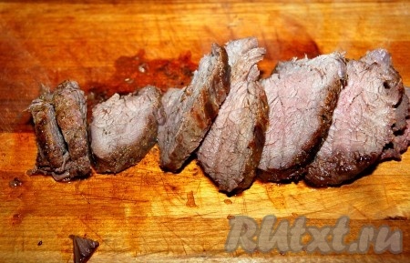 Выложить горячее мясо на деревянную доску и нарезать тонкими ломтиками.