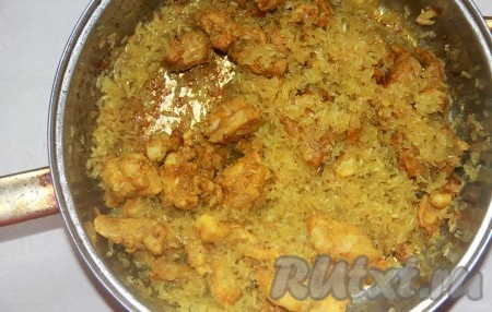 Когда куриное мясо подрумянится, добавляем в сковороду сухой рис. Прожариваем его на сковороде, помешивая, пока рис полностью не впитает в себя всё масло.
