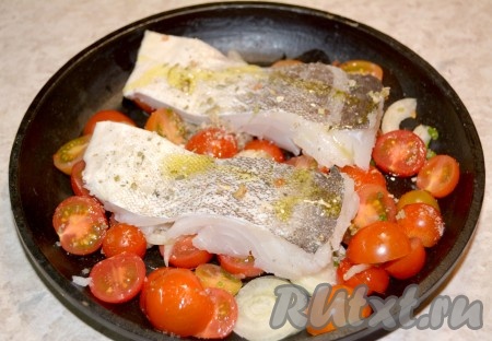 На помидоры с луком выложить кусочки рыбы. Филе рыбы посолить, поперчить, посыпать специями и сбрызнуть оставшимся растительным маслом. Отправить сковородку с рыбой и помидорами запекаться в заранее нагретую до 190 градусов духовку.
