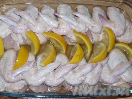 Выложить куриные крылышки в жаропрочную форму и залить их сиропом, равномерно поливая сверху крылья. Дольки лимона выложить на крылышки.