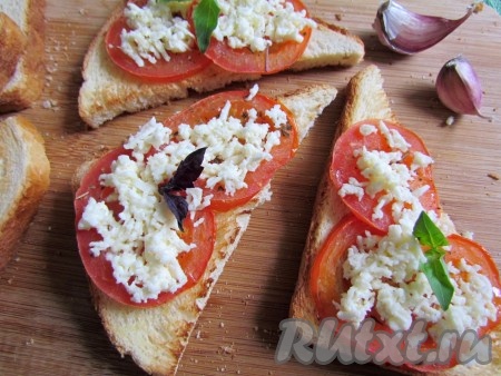 На помидоры положите тертый сыр и украсьте тосты листиками свежего базилика.
