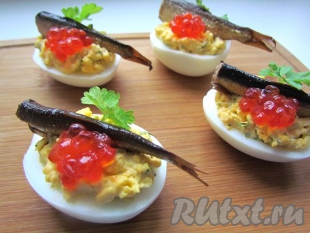 Украсьте фаршированные яйца красной икрой и листиком петрушки.