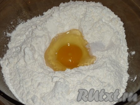 Вначале замесим тесто для чебуреков, для этого в объёмную миску нужно просеять 2,5 стакана муки, сделать в центре углубление, вбить туда яйцо, добавить соль и влить воду.